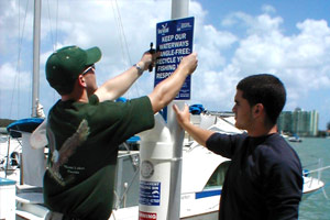 Two boys install a sign which reads, Keep our waterways tangle-free: Recycle your fishing line responsibly.