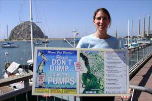 A woman on a dock in California holds a sign which reads - Please Don't Dump...Use The Pumps.