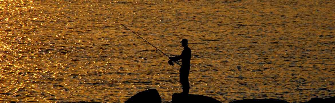 a man fishes as the sun sets on a beach