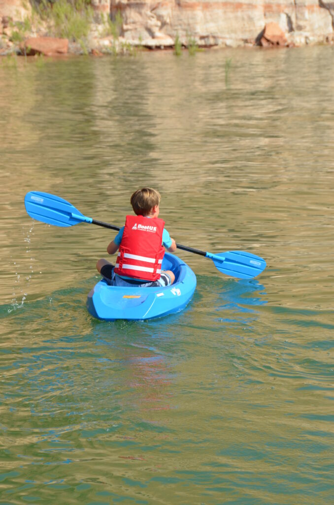 Photo of a boy in a red life jacket paddling in a kayak on a river